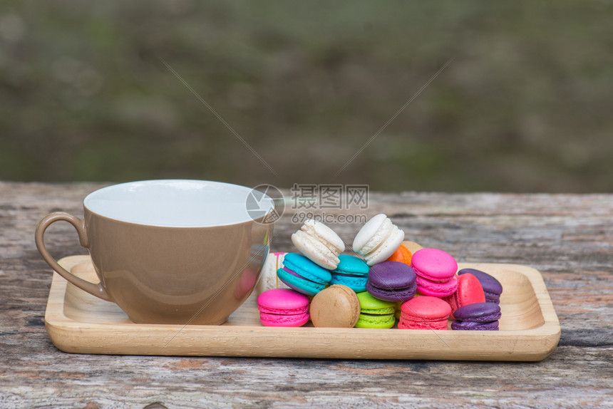 咖啡杯和花彩的麦卡罗翁在菜园的木制桌边盘子上图片