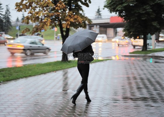 灯在下面树木雨伞的女孩晚上在城里的湿地上行走图片