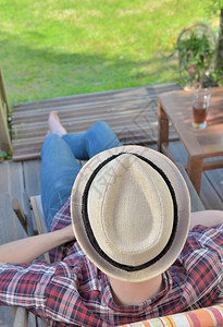 坐着最佳顶部的风景帽子上戴着一名年轻男子穿着夏天在花园里放松甲板图片