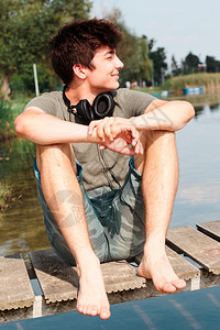 假期坐着在夏天阳光明媚的日子坐在湖边的码头上笑着的男孩儿晴天图片