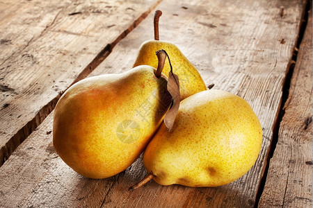 明亮的黄色木制背景上三颗多汁的成熟梨子白色图片