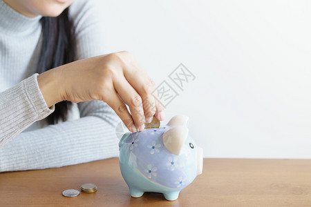 妇女亲手把硬币放进小猪中为投资省钱现金节在室内图片