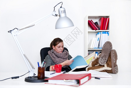 一种书年轻女子不知疲倦地学习翻一个文件夹在桌子上站着她的脚背景是脱白的女士图片