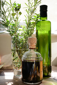 一瓶橄榄油和巴萨醋酸放在装满迷迭香和红菜的杯子旁边史密斯美食草药图片