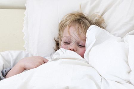 生病的男孩抱起来在睡床上的被子下面温度金发在图片