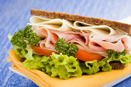 健康毛巾蓝玻璃桌上配有生菜的美味大奶酪和火腿三明治美味的图片
