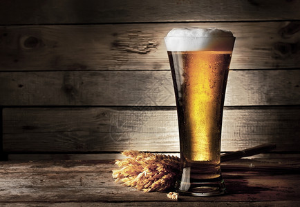 棕色的喝泡沫高架啤酒杯有和木制背景的耳朵图片