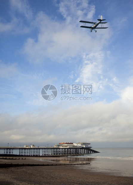 航班旅行在英格兰东南部诺福克海岸罗默的码头和海滩上飞过码头和海滩的老双翼飞机艾伦图片
