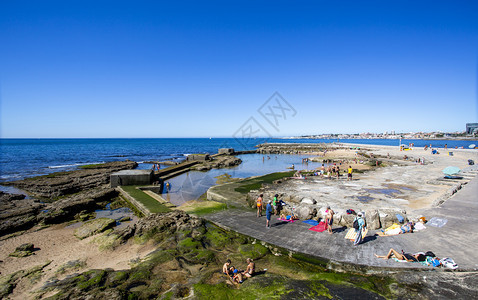 户外建成海洋在葡萄牙埃斯托里尔塔马海滩岩石上建起的游泳池周围人们享受太阳和大西洋环绕着一个游泳池的阳光和大西洋图片