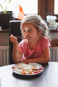 食物真正的小女孩在家吃晚饭餐桌上的盘子吃饭孩拿着叉真实的人情况可口图片