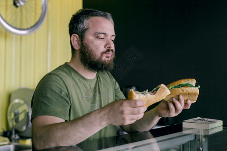 年轻的饿着吃三明治饥饿男人餐厅生图片