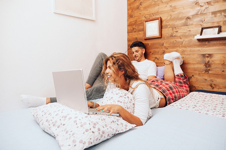 枕头床单微笑着的年轻异恋夫妇躺在床上用笔记本电脑两个都图片