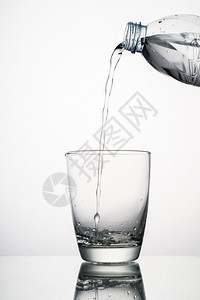 瓶子液体喝从白色隔离的玻璃上溅起倒水特写从在白色背景上隔离的玻璃溅起倒水特写图片