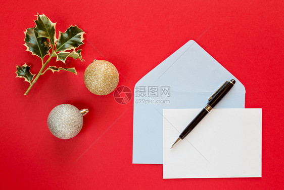 白色的问候超过圣诞信和笔在红色背景上带有装饰品的圣诞信和红色背景上的面图片