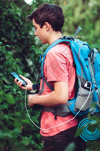 年轻人在徒步时使用线智能电话在旅途中充电移动话手持背包垂直的年轻远足背景图片