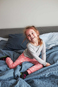 快乐的小玩女孩得开心做傻笑的脸在床上跳早卧室家微笑制造有趣的图片