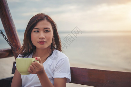 美丽的女人坐在沙滩上喝咖啡放松图片