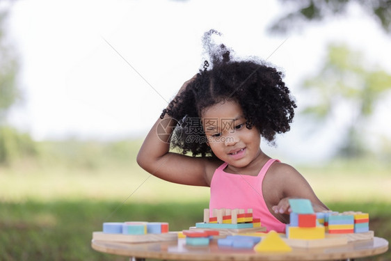 一个黑卷发的女孩坐在她的双手旁加入木锯时抓着头部混淆不清抓挠户外非洲裔图片