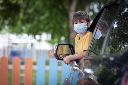 面具小可爱男孩穿着面罩身戴坐在车窗后从前座上车窗撞出孩子在科罗纳大流行疾期间返回学校健康正面图片