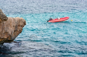 船停泊在西班牙巴利阿里群岛Mallorca的松绿水岩石附近停靠的小红救生艇夏天图片