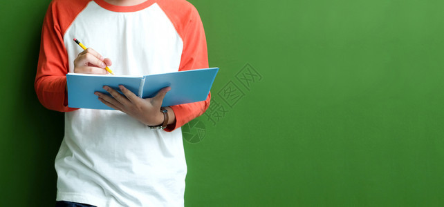 学校文在职的年轻人站绿色墙背景教育横幅面前在笔记本纸上写作的青年男子图片