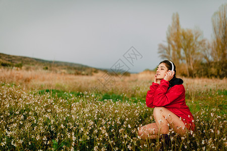 女孩在野花中听音乐耳机响起树多云的春天图片