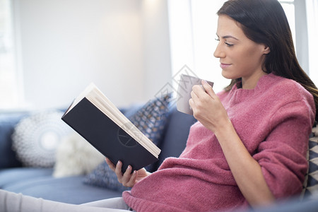 在家索法沙发上喝热饮料放松休闲的妇女阅读书保持轻松识字图片