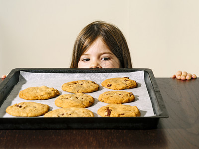 可爱的芯片一个年轻女孩在烤箱外看着一盘温暖的巧克力薯片饼干的照出去图片