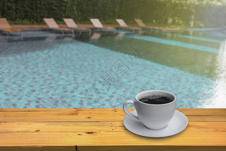 游客白色的咖啡店木地板上一小杯咖啡和模糊游泳池底背景图片