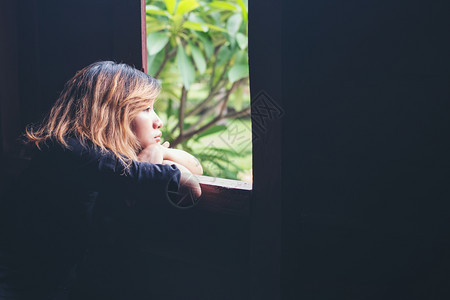 坐在窗边长椅上的年轻悲伤女士向外望去悲伤孤独女生活方式概念坐在长凳上悲伤的年轻妇女打蜜蜂独自的黑发坐着图片