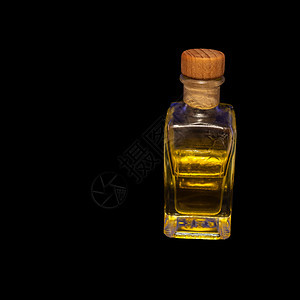 透明矩形玻璃瓶内装一个软木阻塞器半满含光黄色液体在黑背景下发光的黑色圆形图片