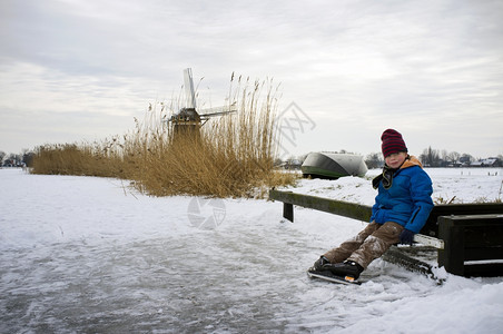 小男孩在冰滑之旅中躺在小码头上冰冻的荷兰运河上芦苇练习灰蒙图片