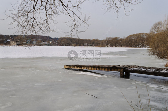 人行道乏味的冰冻湖面覆盖着积雪远处有平板脚路村寒冷的图片