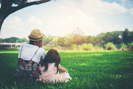 年轻母亲和女儿坐在公园绿草地上放松在公园里休息女士孩坐着图片