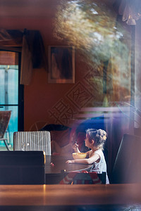 房间可爱的小女孩吃早餐小可爱的女孩坐在桌边吃早餐一玻璃窗里的反射人真正的瞬间实情况坦率坐着图片