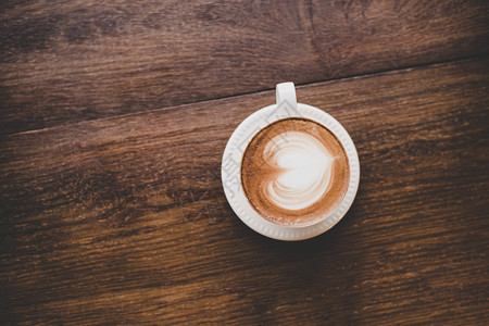 颜色早餐陈年拿铁艺术咖啡的顶端视图木制成心形旧拿铁艺术咖啡的顶端视图木制桌子上的心脏形状牛奶图片