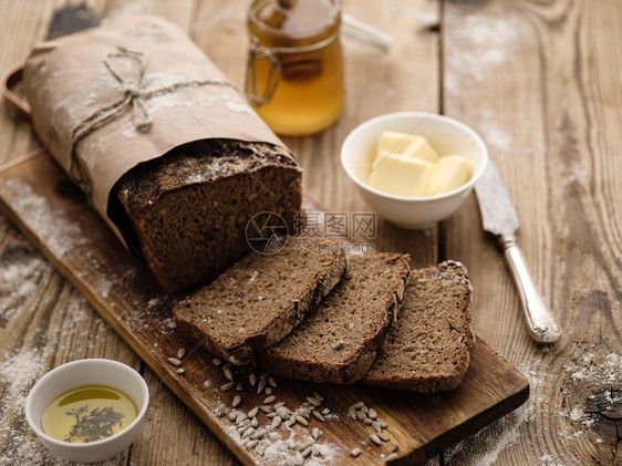 用黄油和蜂蜜在木背景上切成自制黑麦面包棕色的新鲜吃图片