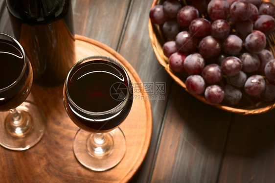 酒鬼用红球葡萄和一瓶酒的红葡萄玻璃杯用天然光聚焦点在暗木上拍照选择焦点关注葡萄酒杯的边缘重点图片
