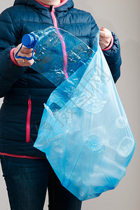 出去女收集蓝色塑料袋废物中的空压碎瓶子以回收塑料污染概念和废物过多的概念在垃圾桶中丢弃废旧塑料瓶和包装物的妇女扔弃废旧塑料瓶和包图片