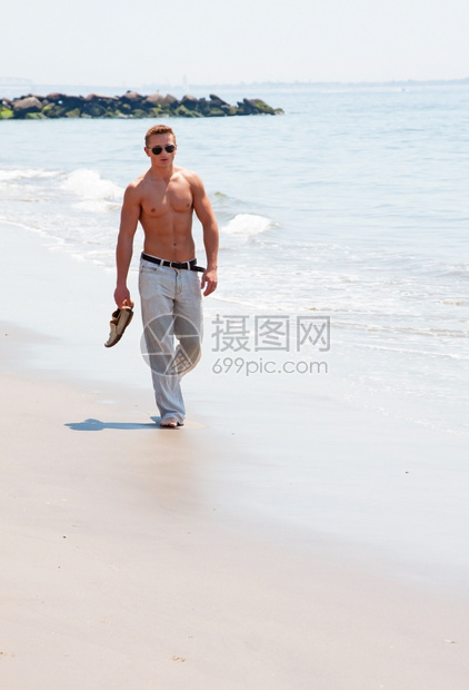 海洋晴天躯干在滩上散步的可爱帅哥身躯体6包腹肌手握着鞋子戴墨镜图片