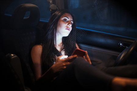 里面日落坐在车的年轻女士使用她的智能手机看着窗子天气图片