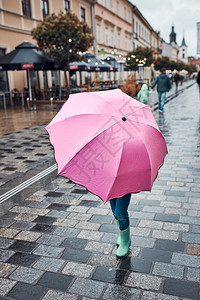 落下躲在粉红色大伞后的小女孩在阴雨沉的秋日在市中心散步走一种图片