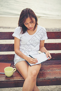 铅笔绘画年轻美女在沙滩上放松时坐在长椅上用笔记本写字事图片