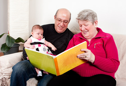 女自豪的和快乐祖父母阅读书教育她们的孙女婴儿孩在客厅沙发上坐着时享受书本乐趣背景图片