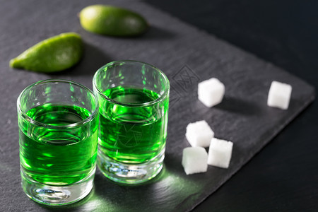 眼镜绿色一杯苦艾酒加石灰和糖在黑色背景上一杯苦艾酒加石灰和糖鸡尾酒图片