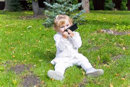 卷发白种人手机坐在绿草地上的小可爱女婴淑图片