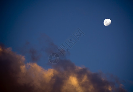 几乎满的白月亮在乌云最后光芒下升起夜晚蓝色的黄昏图片