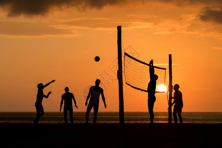 夕阳下在沙滩边打排球的人们背景图片