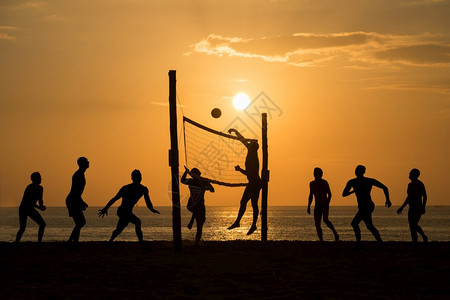 排球剪影夕阳下在沙滩边打排球的人们背景