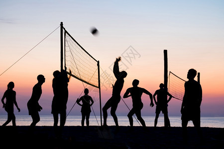 夕阳下在沙滩边打排球的人们背景图片